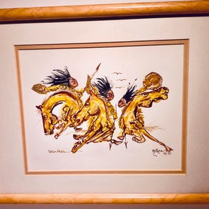 May include: Framed watercolour painting depicting Native American figures on horseback. The artwork shows three riders on golden horses, with feathered headdresses and spears. The painting has a dynamic style, with the artist's signature in the lower corners.