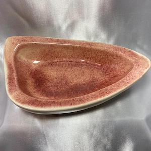 May include: A mid-century modern, ceramic serving dish. The dish is a unique, asymmetrical shape with a speckled, reddish-brown interior and a cream-colored rim. The dish is approximately 12 inches long.