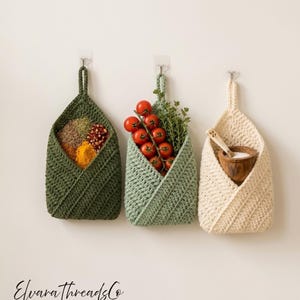May include: Three hanging crochet baskets in dark green, sage green, and cream. The dark green basket holds various spices, the sage green basket contains cherry tomatoes and herbs, and the cream basket holds a wooden bowl with a small spoon.