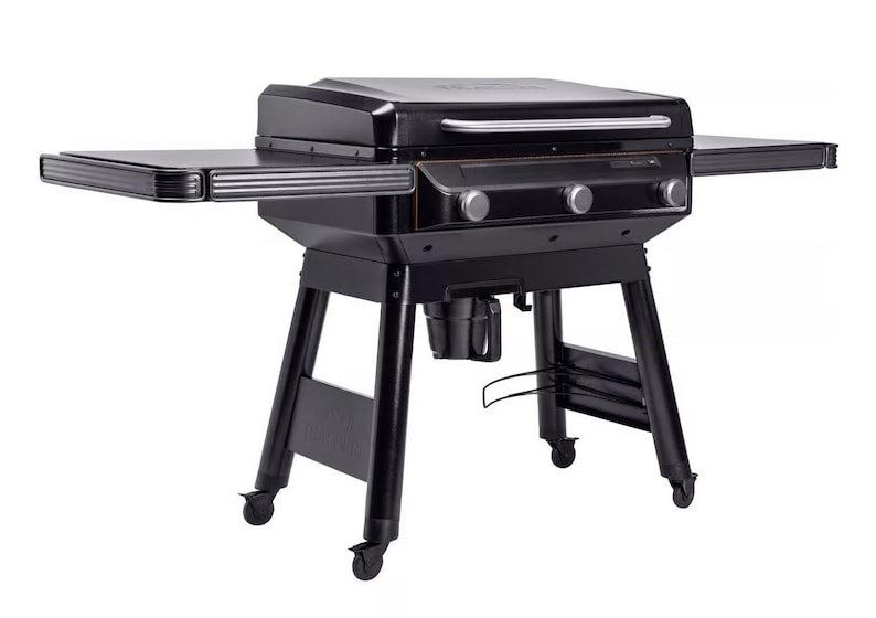 Puede incluir: Una parrilla negra para exteriores con tapa, estantes laterales y perillas de control. La parrilla tiene un asa de acero inoxidable y se asienta sobre un marco de metal negro con ruedas. Los estantes laterales brindan espacio adicional.