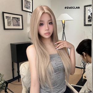 May include: A long, light blonde wig with a natural-looking hairline. The wig is styled with straight, flowing hair. The person in the image is wearing a gray tube top. The text "OZWIGLAB" is visible in the upper right corner.