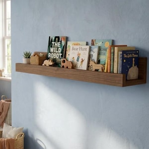 May include: A nursery scene with a light blue wall, featuring a wooden crib, a macrame wall hanging, and a floating shelf. The shelf displays children's books and wooden animal figurines. A rug and a basket are on the floor.