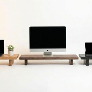 Könnte beinhalten: Drei Monitorständer aus Holz in verschiedenen Farben: hellbraun, dunkelbraun und schwarz. Jeder Ständer hat eine rechteckige Oberseite und kurze, rechteckige Beine. Ein Laptop, ein Desktop-Computer und ein Tablet sind auf den Ständern ausgestellt.