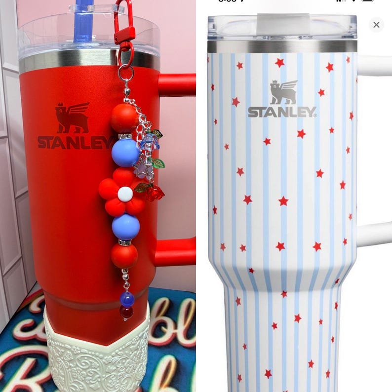 Op de afbeelding: Twee Stanley-bekers. E&eacute;n is rood met een decoratieve bedel. De andere is wit met blauwe strepen en rode sterren. Beide hebben het Stanley-logo en een handvat. De rode beker heeft een witte decoratieve basis.