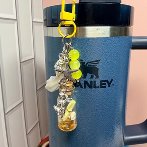 May include: A yellow plastic lobster clasp keychain featuring a silver-toned starfish charm, a small glass bottle with a cork stopper containing a yellow scroll and tiny shells, and three translucent neon yellow beads hanging from a metal ring.