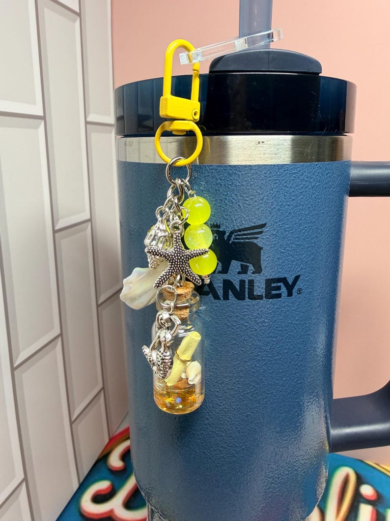 May include: A yellow plastic lobster clasp keychain featuring a silver-toned starfish charm, a small glass bottle with a cork stopper containing a yellow scroll and tiny shells, and three translucent neon yellow beads hanging from a metal ring.