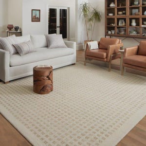 Könnte beinhalten: Ein cremefarbener Teppich mit geometrischem Muster in einem Wohnzimmer. Der Teppich hat ein sich wiederholendes quadratisches Design. Der Raum verfügt über ein weißes Sofa, Ledersessel und einen Beistelltisch aus Holz. Der Raum ist in neutralen Tönen gehalten.