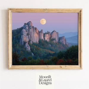 May include: A framed landscape painting depicts a mountain range under a full moon in a twilight sky. The artwork features a gold-colored frame and the text "Moonlit & Laurel Designs" at the bottom.