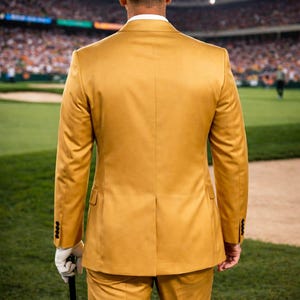 May include: A person wearing a gold suit and a white Titleist cap stands on a golf course, holding a golf club. The background shows a stadium filled with spectators, suggesting a golf tournament.