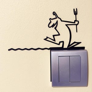 Peut inclure: Décoration murale en métal noir représentant un personnage de dessin animé avec un trident, courant au-dessus d'une ligne ondulée. L'art est monté au-dessus d'un interrupteur argenté à deux boutons rectangulaires, sur un mur crème.