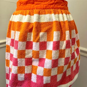 May include: A vintage orange and white checkered towel skirt with a bright orange waistband. The skirt has a pink and white checkered pattern at the bottom.