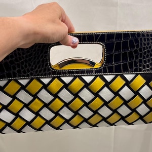 May include: A rectangular clutch bag featuring a black crocodile-embossed frame with a cutout handle. The center panel displays a woven pattern of yellow and white strips. The bag includes a silver-toned metallic accent inside the handle opening.