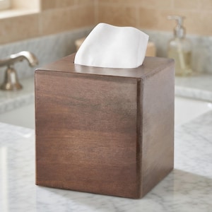 Può includere: Un portatovaglioli quadrato in legno marrone scuro. I fazzoletti bianchi sporgono dalla parte superiore. Il portatovaglioli è posto su una superficie di marmo, suggerendo un accessorio da bagno.
