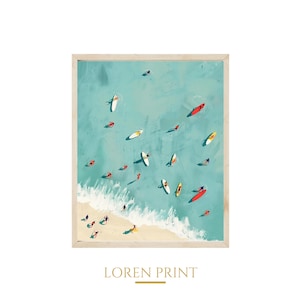 May include: A framed print depicting a beach scene with turquoise water and a sandy shore. Several colorful surfboards and people are scattered in the water. The text "LOREN PRINT" is printed at the bottom of the frame.