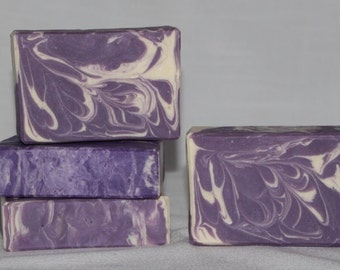 May include: Four bars of handmade soap with a purple and white swirl pattern. The soap is stacked in a pile.