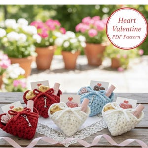 Könnte beinhalten: Eine Sammlung herzförmiger, gehäkelter Geschenktüten in Rot, Weiß und Blau, die jeweils kleine Geschenke enthalten. Die Taschen sind mit einem Band und einem Schlüsselanhänger gebunden. Der Text "Heart Valentine PDF Pattern" ist enthalten.