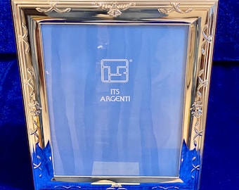 Puede incluir: Un marco de fotos dorado con interior azul. El marco tiene forma rectangular con detalles decorativos florales y de cinta. El texto "ITS ARGENTI" es visible sobre el fondo azul.