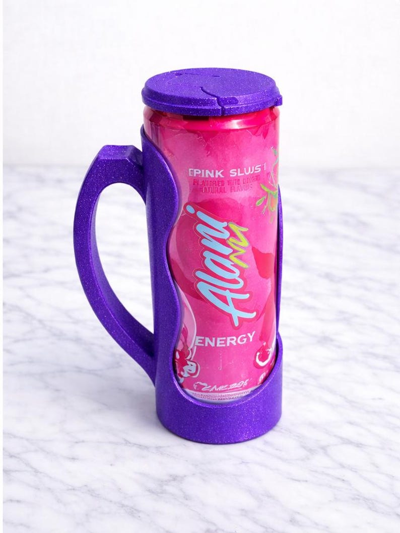 Op de afbeelding: Een paarse blikjeshouder met een handvat, met een roze Alani Energy-blikje. Het blikje heeft de tekst "Pink Slush" en "Energy". De houder heeft een bijpassende paarse deksel.