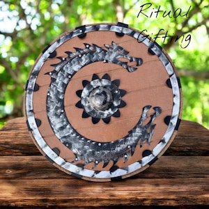 May include: Round wooden shield with a brown center and a silver and black dragon design. The shield has a silver and black border and the text "Ritual Gifting" in the upper right corner.