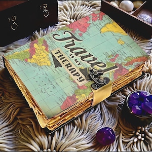Könnte beinhalten: Ein Vintage-Reisetagebuch mit Weltkarten-Design auf dem Cover, mit dem Text "Travel is my Therapy". Das Tagebuch ist mit einem Metallverschluss und einem goldfarbenen Riemen gesichert. Die Seiten haben ein abgenutztes Aussehen.