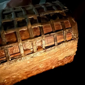 May include: A decorative wooden chest with metal accents. The chest has a rectangular shape with a curved top and is constructed with wooden planks and metal bands. The exterior has a weathered appearance, suggesting age or a vintage style. The chest is partially lit, with a dark background.