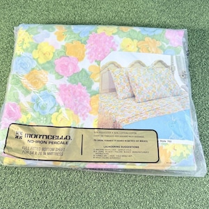 May include: A Monticello no-iron percale full fitted bottom sheet for a 54 by 76 inch mattress, packaged in clear plastic. The fabric features a floral pattern with pink, yellow, and blue flowers on a white background, shown in an inset image.