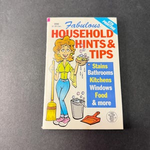 May include: A vintage paperback book titled Fabulous Household Hints & Tips with a cartoon illustration of a person holding a broom and a sponge. The cover features text listing topics like stains, bathrooms, kitchens, windows, and food.