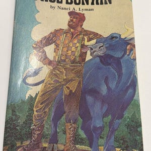 May include: A vintage book cover titled "Paul Bunyan" by Nanci A. Lyman. The illustration features a lumberjack in a plaid shirt and suspenders, standing next to a large blue ox. The background includes a blue sky and green trees.