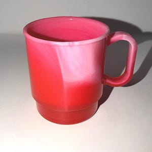 May include: A red and pink mug with a handle. The mug has a layered design, with the bottom and handle being a solid red color. The middle section is a mix of pink and white, and the top is a lighter pink.