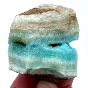 May include: A natural stone specimen with layers of brown, white, and turquoise blue. The stone has a rough, textured surface and a hole through the center. The colors are vibrant and the layers are clearly visible, creating a unique and eye-catching appearance.