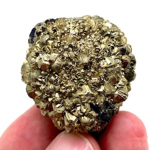 Op de afbeelding: Een gouden pyrietcluster met een kristallijne structuur. Het mineraalmonster heeft een metaalglans en een ruw, getextureerd oppervlak. De pyriet heeft een messinggele kleur, met enkele donkerdere plekken. De cluster wordt tegen een witte achtergrond gehouden.