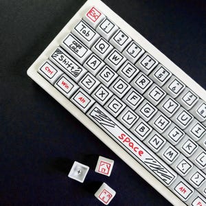 May include: A white keyboard with black outlined keys and red accents. The keys are labeled with letters, numbers, and symbols. The space bar has the word "Space" in red. Several loose keys are scattered below the keyboard.