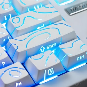 May include: Close-up of a white mechanical keyboard with blue LED backlighting. The keycaps have a unique design with blue illuminated lines. The "Shift" and "Ctrl" keys are visible, along with other function keys. The keyboard has a modern aesthetic.