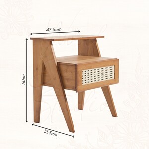 Puede incluir: Una mesita de noche de estilo moderno de mediados de siglo hecha de madera marr&oacute;n claro. La mesita tiene un caj&oacute;n con frente de mimbre tejido y patas anguladas. Dimensiones: 47,5 cm de ancho, 50 cm de alto y 31,5 cm de profundidad.