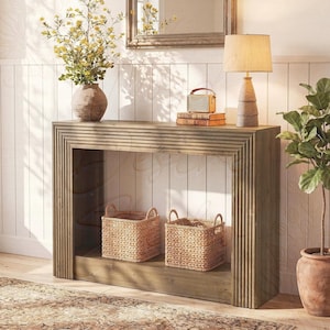 Puede incluir: Una mesa consola rectangular de madera con detalles estriados verticales en el marco y las patas. La mesa cuenta con un estante inferior que sostiene dos cestas de mimbre tejidas. Una lámpara color canela, una radio pequeña y un florero.