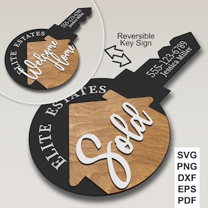 May include: A black and wood-toned key-shaped sign with the words "Welcome Home" and "Sold" in white script. The sign includes the text "Elite Estates" and a phone number. The sign is reversible.