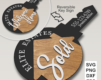 May include: A black and wood-toned key-shaped sign with the words "Welcome Home" and "Sold" in white script. The sign includes the text "Elite Estates" and a phone number. The sign is reversible.