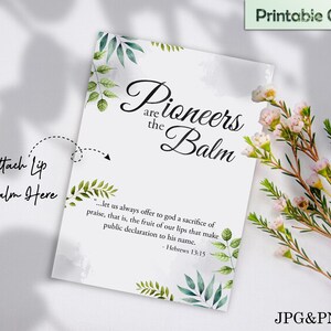 May include: A white printable card with the text "Pioneers are the Balm" in elegant script, adorned with watercolor-style green leaves. The card includes the text "...let us always offer to god a sacrifice of praise..." and the words "Attach Lip Balm Here".