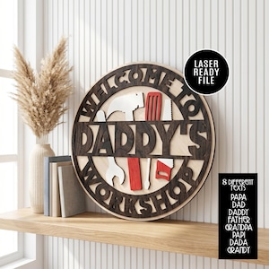 May include: A wooden sign with the words "WELCOME TO DADDY'S WORKSHOP" cut out in a dark brown color. The sign features tools in red, white, and brown. A black circle indicates a laser-ready file. The sign is on a wooden shelf.