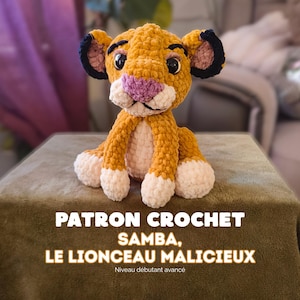 Può includere: Un cucciolo di leone all'uncinetto con pelliccia dorata, petto e zampe color crema e naso rosa. Il giocattolo ha grandi occhi neri e orecchie con punte scure. Il testo recita: PATRON CROCHET SAMBA, LE LIONCEAU MALICIEUX, Niveau débutant avancé.