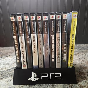 May include: A black plastic display stand with the white PS2 logo holding ten PlayStation 2 video game cases. The titles include Grand Theft Auto III, Winning Eleven 10, Sengoku Basara, Kingdom Hearts, Final Fantasy XI, and Metal Gear Solid 3.