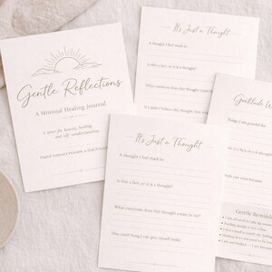 Może przedstawiać: Kolekcja minimalistycznych dzienników uzdrawiających z tytułem "Gentle Reflections" i podpowiedziami takimi jak "It's Just a Thought" i "Gratitude Without Guilt". Dzienniki leżą na neutralnej powierzchni, z filiżanką kawy i dekoracyjnymi kwiatami.