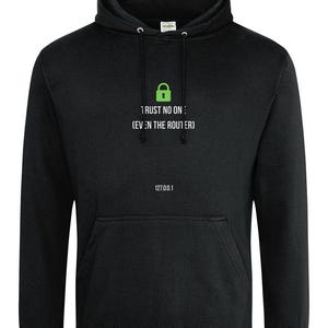 Puede incluir: Sudadera con capucha negra con bolsillo delantero y capucha con cordón. La parte delantera presenta un icono de candado verde y el texto "1 RUST NO ONE: (EVEN THE ROUTER)" y "127.0.0.1" en blanco. Una prenda casual y cómoda.