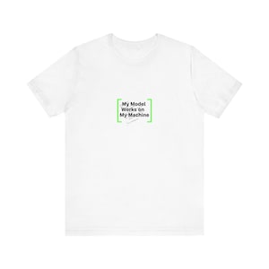 Op de afbeelding: Een wit t-shirt met de tekst "My Model Works on My Machine" in een groene rechthoekige kader. De tekst is in een schreefloze lettertype. Het shirt is gemaakt van een zacht materiaal.