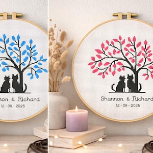 May include: Cross-stitch hoop art featuring a tree with blue leaves and two black cats. The names "Shannon & Richard" and the date "12-09-2025" are stitched below. The artwork is displayed with a candle and books.