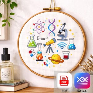 May include: A cross-stitch embroidery hoop featuring a science-themed design. The design includes a purple atom, a DNA strand, a microscope, a telescope, beakers, pills, and the equation E=mc². The hoop is made of wood and has a gold-colored hanging mechanism.