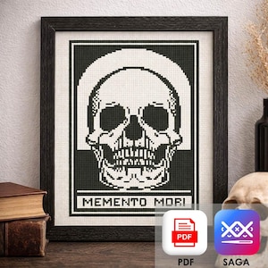May include: Black framed cross-stitch art featuring a skull design. The skull is white against a black background, with the words "MEMENTO MORI" at the bottom. The artwork is displayed on a white background.