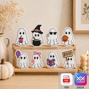 May include: A set of eight white ghost cross-stitch patterns displayed on a two-tier wooden stand. The ghosts feature various accessories including a witch hat, a cauldron, sunglasses, a pumpkin, a purple balloon, a pink bow, a book, and a sign reading BOO!