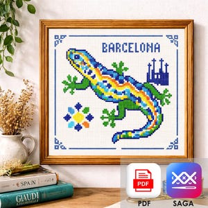 May include: Cross-stitch art of a colorful lizard with the word "BARCELONA" above it. The lizard is blue, green, yellow, and orange. The artwork is framed in a wooden frame and includes a blue border with decorative elements.