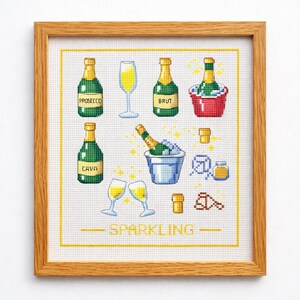 May include: Cross-stitch artwork in a wooden frame featuring champagne bottles, glasses, and ice buckets. The bottles are labeled "Prosecco", "Brut", and "Cava". The word "Sparkling" is stitched at the bottom.
